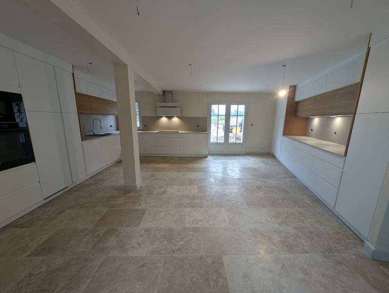 Cuisine blanc mat et bois massif sans poignée avec double rangée de meubles hauts, plan de travail céramique beige calcaire et colonnes hautes à Castres-Gironde près de Bordeaux